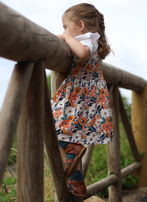 Child in a floral dress standing on a wooden structure with a natural background